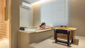 A spa room with a bathtub, a wooden table, and a window with blinds. - Anook Hotel Daejeon Munchang (Daejeon)