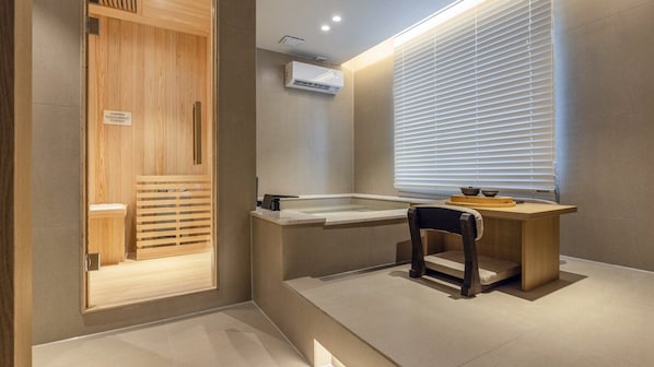 A modern bathroom with a wooden shower enclosure, a bathtub, and a window with blinds.