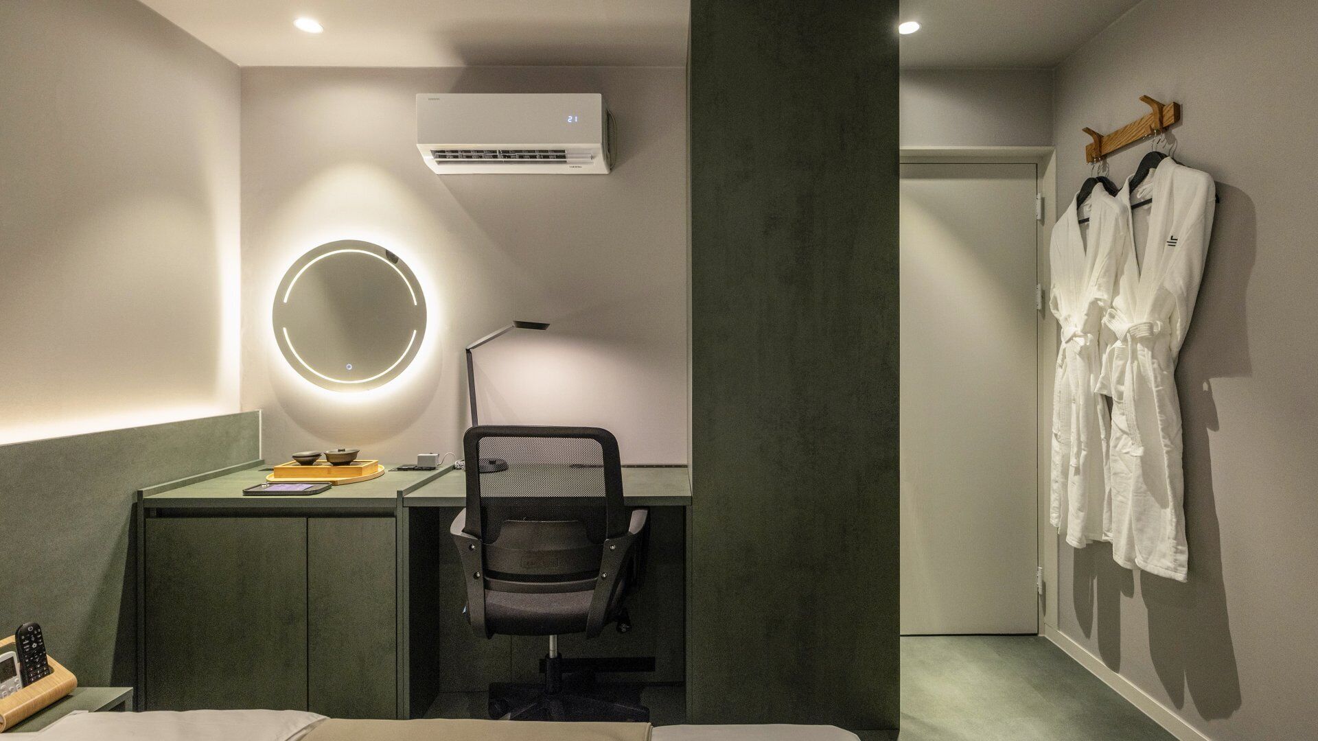 Habitación de hotel con escritorio, silla, aire acondicionado, bata y cama.
