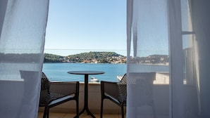 A balcony with a table and two chairs, overlooking a body of water and a hillside town. - Hotel M (ZATON)
