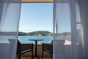 Ein Balkon mit Tisch und zwei Stühlen, der auf ein Gewässer und eine Hügelstadt blickt.