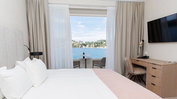 A hotel room with a bed, a desk, a chair, a TV, and a view of the sea. - Hotel M (ZATON)