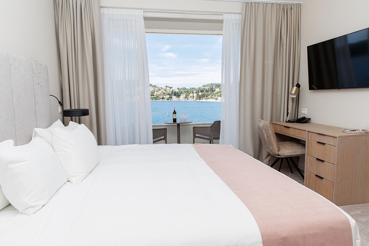 Ein Hotelzimmer mit Bett, Schreibtisch, Sessel, Fernseher und Meerblick.