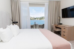 A hotel room with a bed, a desk, a chair, a TV, and a view of the sea. - Hotel M (Dubrovnik)