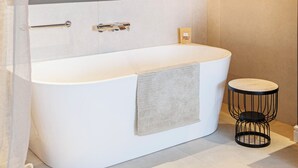 A modern bathroom with a freestanding bathtub, a towel rack, a small round table, and a hanging light fixture. - Hotel M (ZATON)