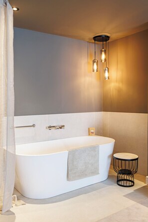 Ein modernes Badezimmer mit einer freistehenden Badewanne, einem Handtuchhalter, einem kleinen runden Tisch und einer hängenden Leuchte.