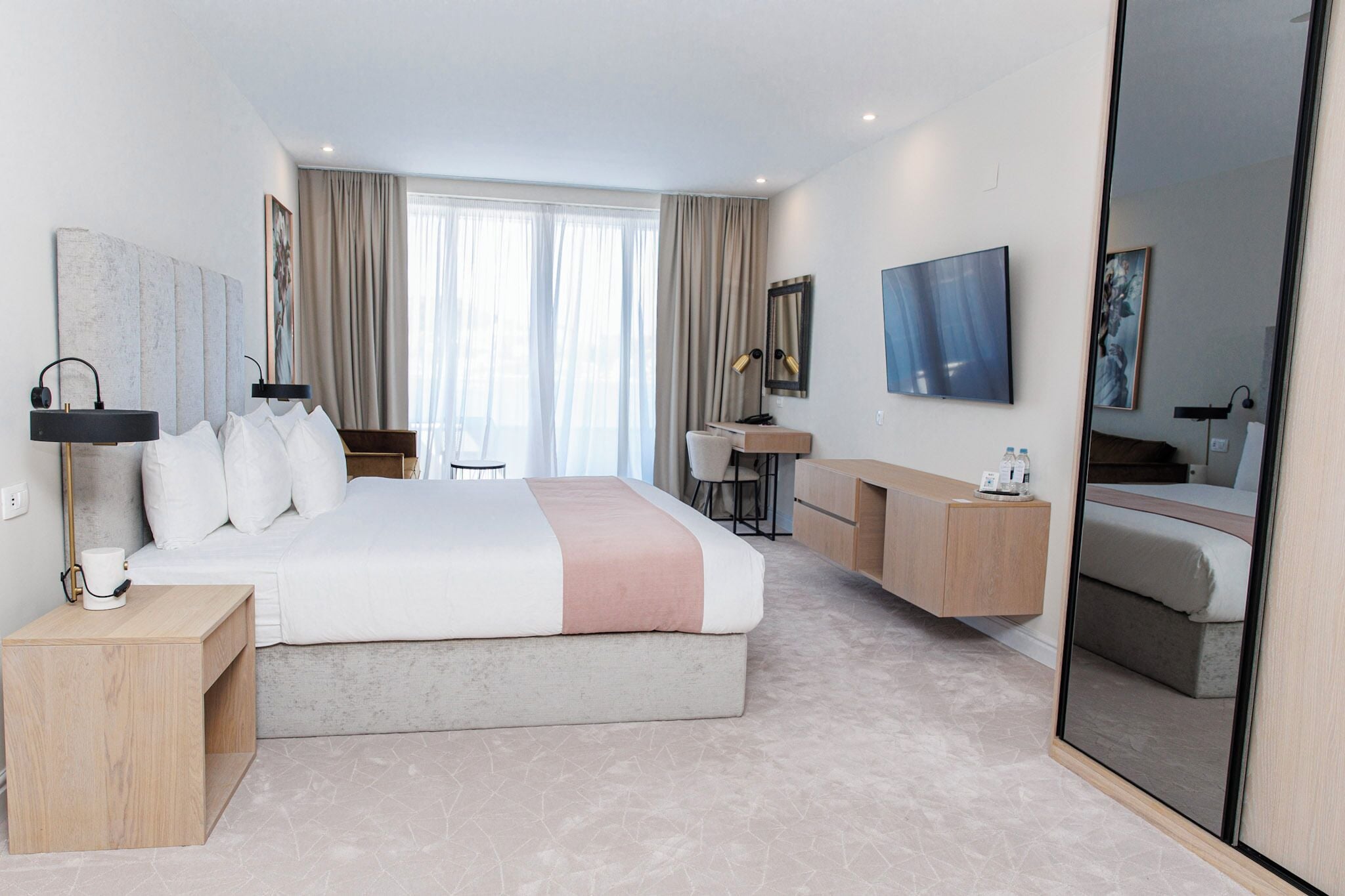 Ein modernes Hotelzimmer mit einem großen Bett, einem Schreibtisch, einem Sessel, einem Fernseher und einem Spiegel.