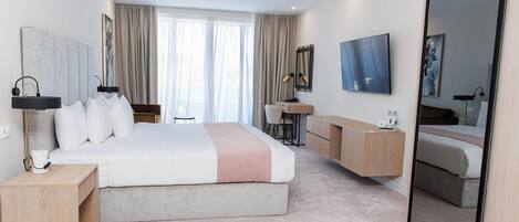 Ein modernes Hotelzimmer mit einem großen Bett, einem Schreibtisch, einem Sessel, einem Fernseher und einem Spiegel.