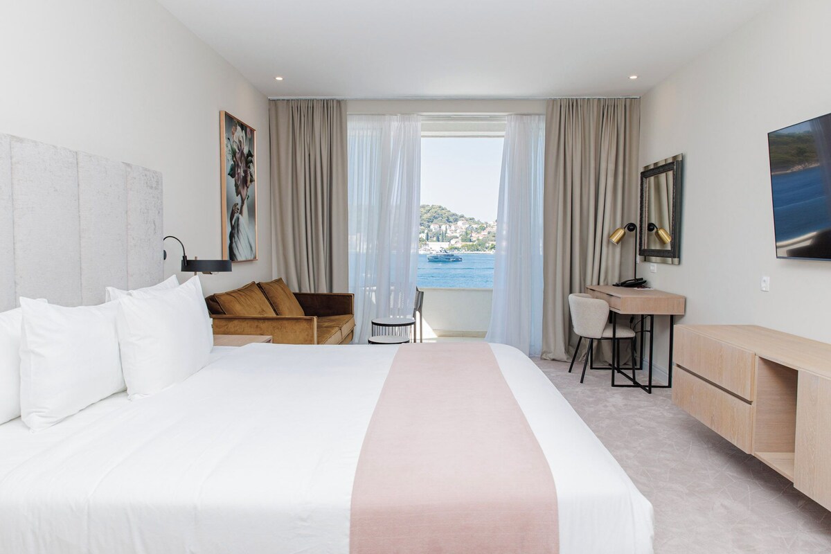 Ein Hotelzimmer mit einem großen Bett, einem Schreibtisch und Meerblick.