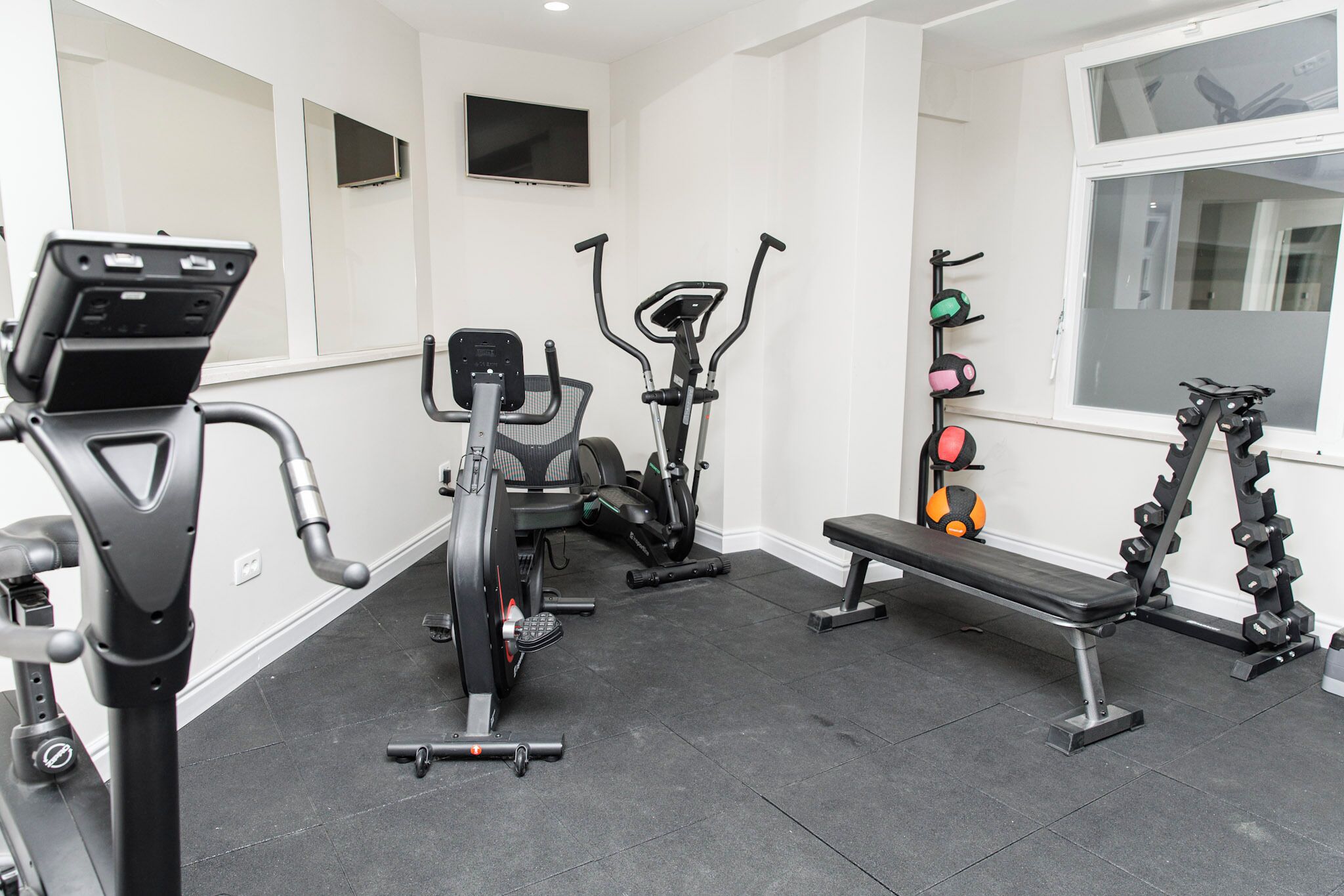 Un gimnasio con equipo de ejercicio, incluyendo una cinta de correr, bicicleta estática, elíptica, banco y un estante para pesas.