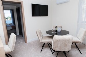Ein Zimmer mit einem runden Tisch, vier Stühlen, einem Fernseher an der Wand und Blick ins Freie.