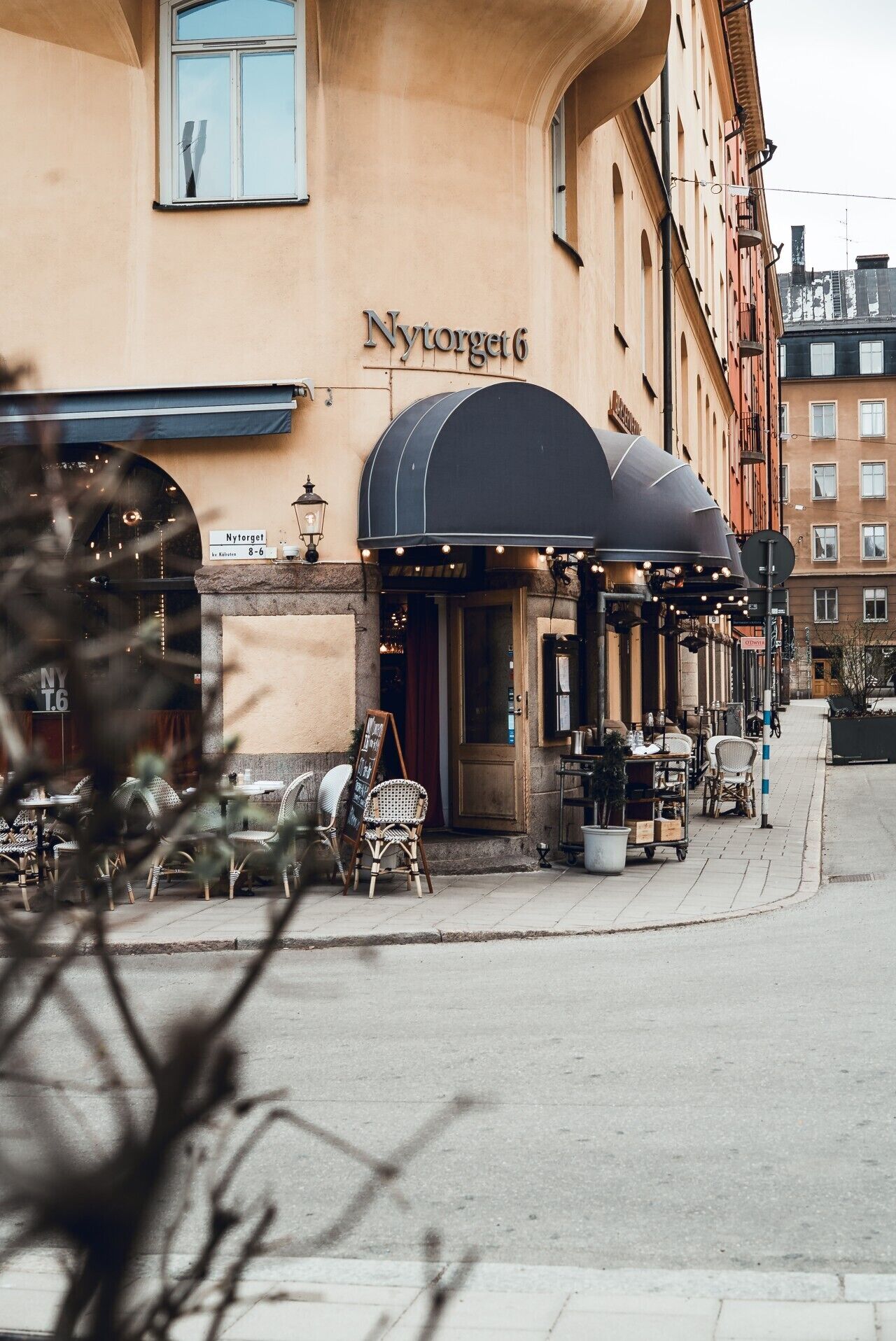 Ett utomhusområde med bord och stolar framför en byggnad där det finns en skylt med texten ”Nya torget 6”.