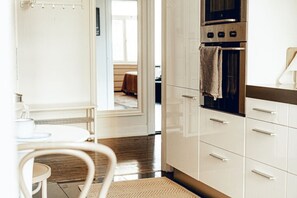 Eine moderne Küche mit weißen Schränken, einem eingebauten Ofen und einem Essbereich mit einem weißen Tisch und Stühlen.