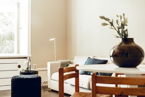 Ein Wohnzimmer mit einer Couch, einem runden Tisch, einer Vase mit Blumen und einer Lampe.