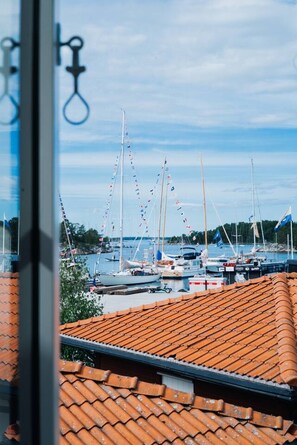A marina with multiple sailboats docked, a clear sky, and a tiled roof in the foreground. - Royal Yacht Club Apartment — Sandhamn Harbour (Sandhamn)