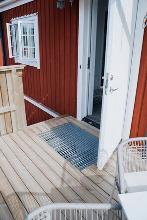 A wooden deck with a metal grate entrance, a white door, and a small wooden structure to the left. - Royal Yacht Club Apartment — Sandhamn Harbour (Sandhamn)