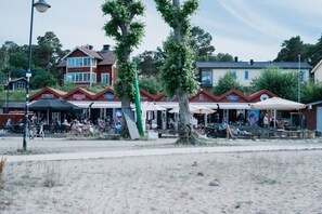 A beachfront area with outdoor seating at a restaurant, bicycles parked, and a sandy foreground.
