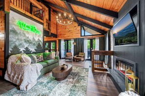 Interior acolhedor de uma cabana com um letreiro de néon verde, lareira e uma grande janela com vista para uma floresta.