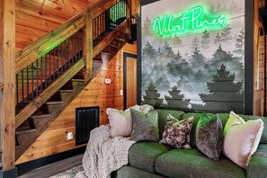 Uma escada de madeira com um letreiro de neon que diz 'Velvet Pines' acima de um sofá verde com várias almofadas.