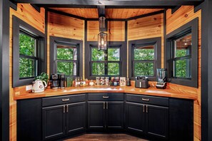Eine moderne Küche mit schwarzen Schränken, Holz Arbeitsplatten und großen Fenstern mit Blick auf Bäume.