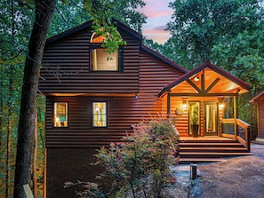 A log cabin with a porch, a staircase leading to the entrance, and a view of the surrounding forest. - Velvet Pines | Lake Front | Amenities Galore | 5* (Pigeon Forge)