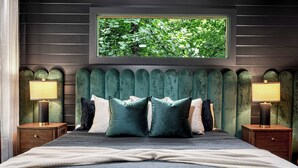A bedroom with a large bed, two nightstands, a window with a view of greenery, and a green upholstered headboard. - Velvet Pines | Lake Front | Amenities Galore | 5* (Pigeon Forge)