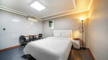 Habitación de hotel con una cama grande, un escritorio con dos sillas, aire acondicionado de pared, un cuadro enmarcado y una lámpara de noche.