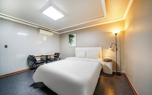 Habitación de hotel con una cama grande, un escritorio con dos sillas, aire acondicionado de pared, un cuadro enmarcado y una lámpara de noche.