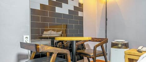 A small room with a wooden table and chairs, a lamp, a speaker, and a wall with a geometric tile pattern.