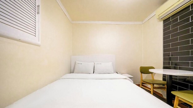 A small, single-bed room with a white bed, a small round table, and two chairs.