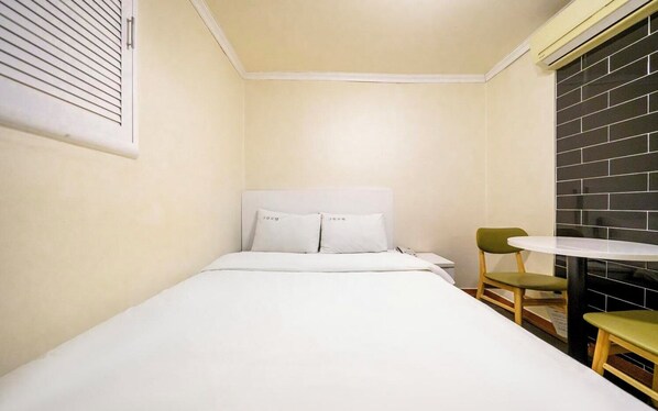 A small, single-bed room with a white bed, a small round table, and two chairs.