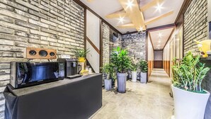 A reception area with a black counter, a Samsung microwave, a coffee machine, and several potted plants.