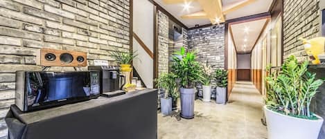 A reception area with a black counter, a Samsung microwave, a coffee machine, and several potted plants.