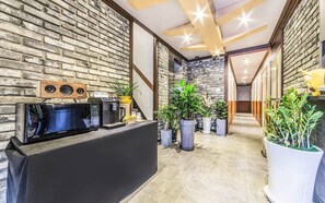 A reception area with a black counter, a Samsung microwave, a coffee machine, and several potted plants.