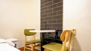 A small room with a bed, a bedside table, a chair, a small table, and a wall with black tiles.