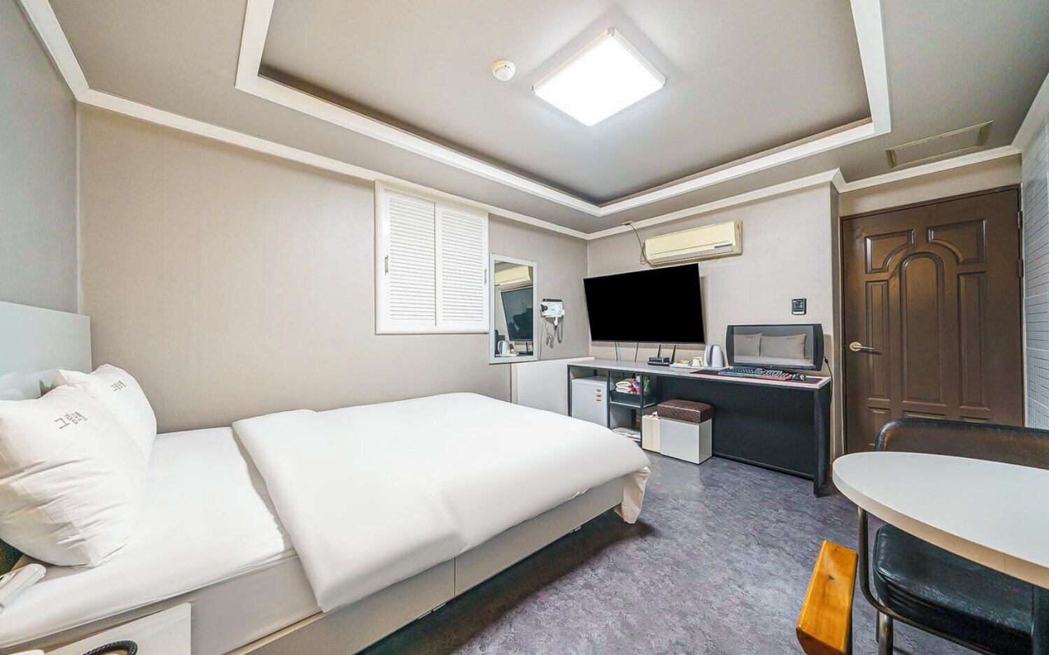A hotel room with a bed, desk, television, and a door.