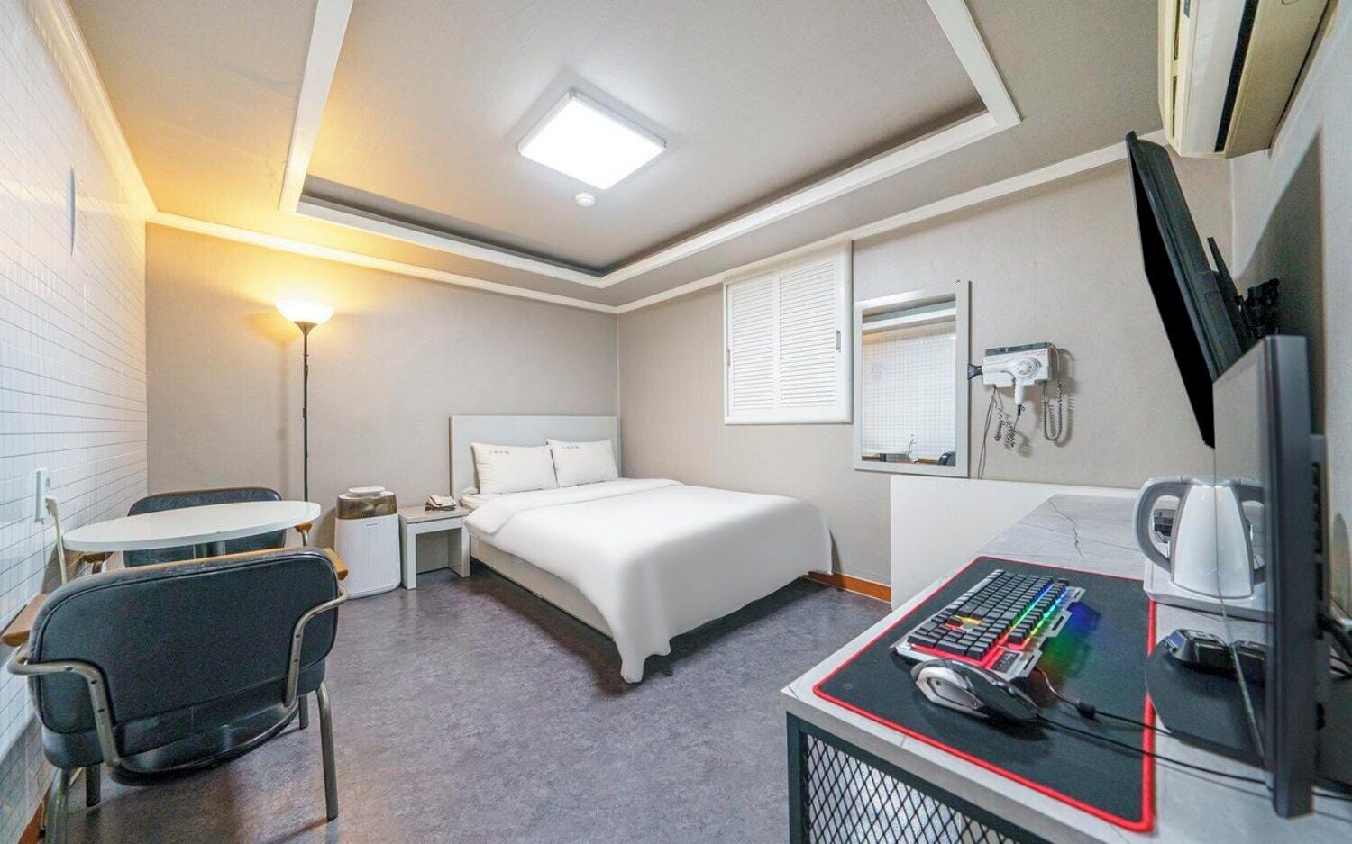 A hotel room with a bed, a desk with a computer, a chair, a lamp, and a telephone.
