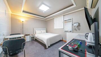 A hotel room with a bed, a desk with a computer, a chair, a lamp, and a telephone.