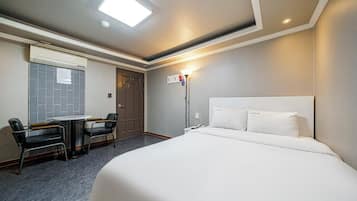 A hotel room with a bed, a desk, a chair, a window, and a door.