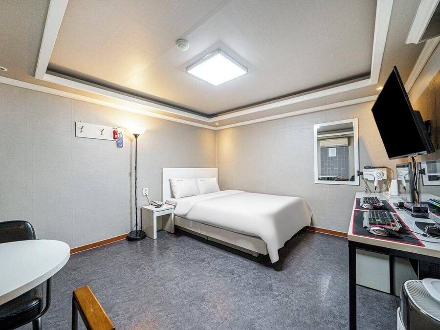 A hotel room with a bed, desk, chair, and a flat-screen TV.