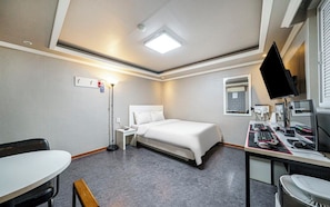 A hotel room with a bed, desk, chair, and a flat-screen TV.