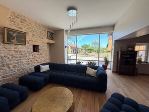 Ein Wohnzimmer mit Steinwand, großem Fenster, einem dunkelblauen Modulsofa und Holzboden.