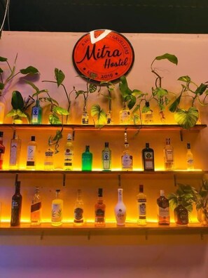 Un minibar con varias botellas de licor y un cartel que dice 'Mitra Hostel' con la fecha 'ESTD 2019'.