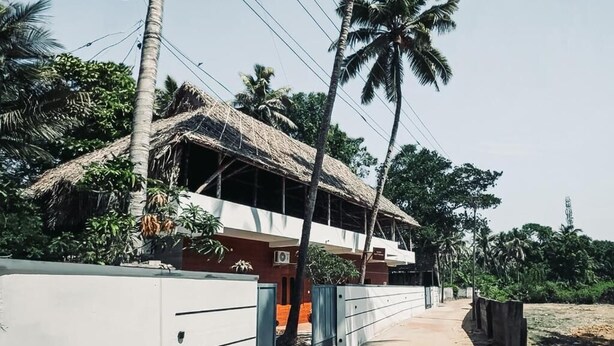 Una casa con techo de paja, rodeada de palmeras y un muro de concreto.