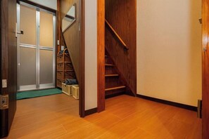 A wooden staircase leading to a second floor, a wooden door with a sliding glass panel, and a green mat at the entrance. - Tokyo Star House-Shinkoiwa (Katsushika City)