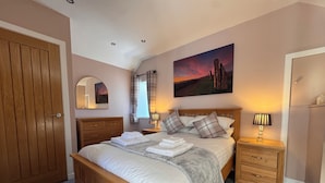 Une chambre à coucher avec un lit en bois, une table de chevet, un miroir, une fenêtre avec des rideaux et un tableau accroché au mur.