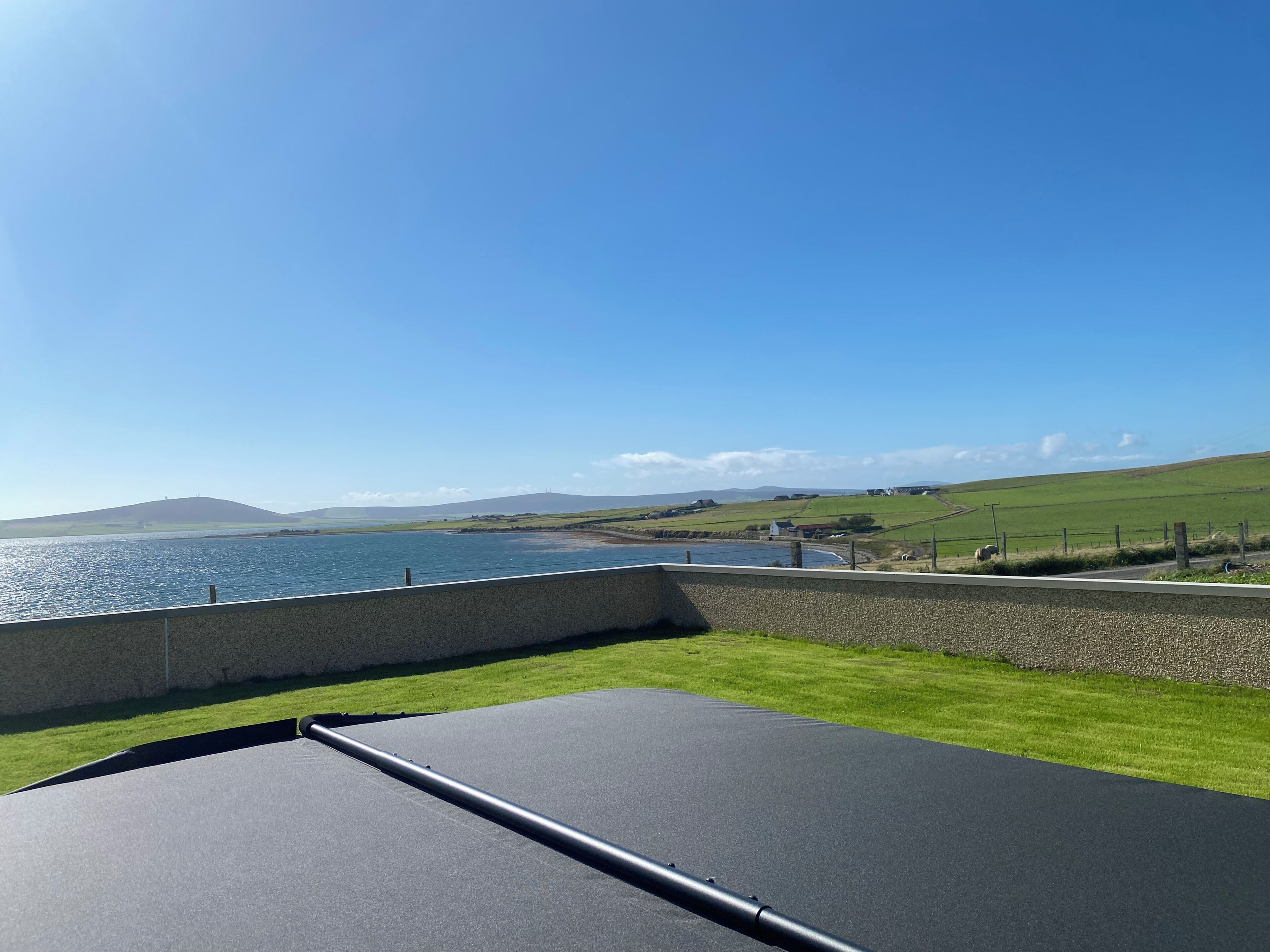 A view from a balcony overlooking a body of water with a grassy area and a stone wall.