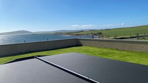 Une vue depuis un balcon donnant sur une étendue d’eau, avec une zone herbeuse et un mur de pierre.