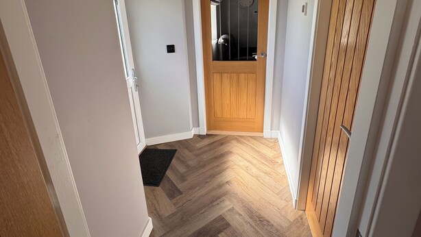 Un couloir avec un plancher en bois, une porte en bois et un porte-manteau.