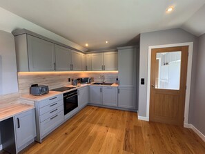 Eine moderne Küche mit grauen Schränken, einer Holz Arbeitsplatte, einem Backofen, einer Spüle und einer Tür mit Spiegel.